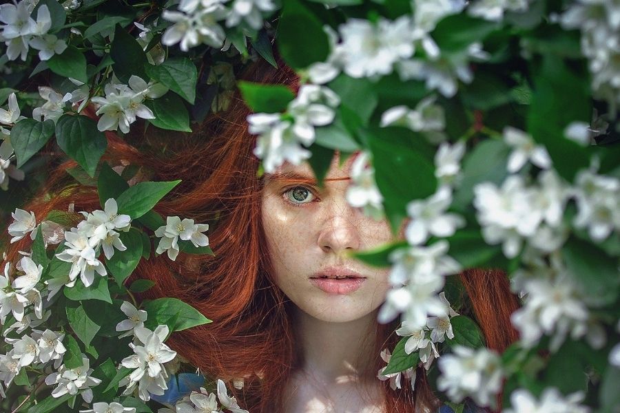 草花から覗き込む赤毛の女性
